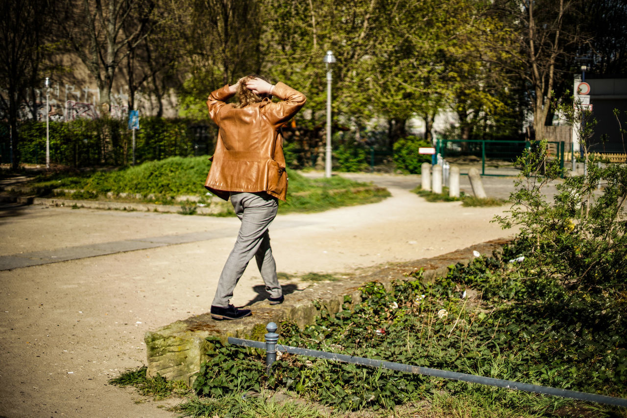 tree, plant, one person, full length, rear view, casual clothing, day, real people, nature, standing, leisure activity, lifestyles, adult, young adult, walking, motion, transportation, city, footpath, outdoors, shorts