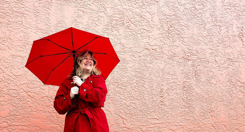 Midsection of woman holding umbrella standing against wall