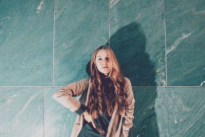 Portrait of young woman standing against wall