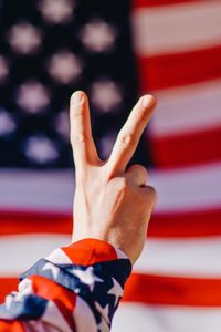 Cropped hand gesturing peace sign against american flag