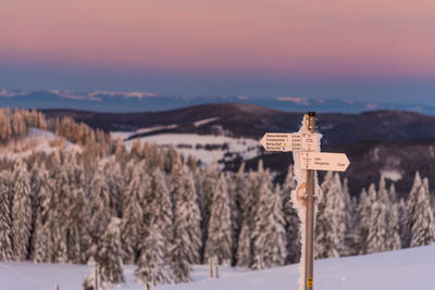 Cross on snow covered mountains against sky during sunset