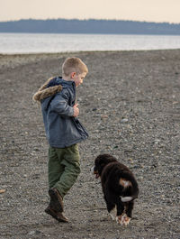 Side view of boy playing with dog at beach