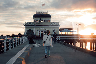 Rear view of man standing on pier against sky during sunset