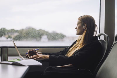 Female entrepreneur sitting with laptop in ferry while looking out through window
