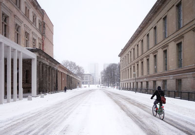 People riding motorcycle on road amidst buildings against sky in city