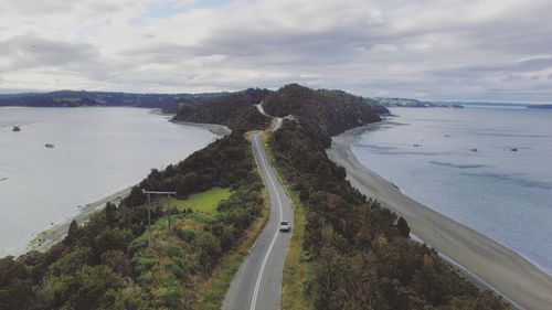 Vehicle on road amidst trees by sea against sky