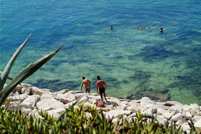 High angle view of shirtless men on rocks against sea during sunny day