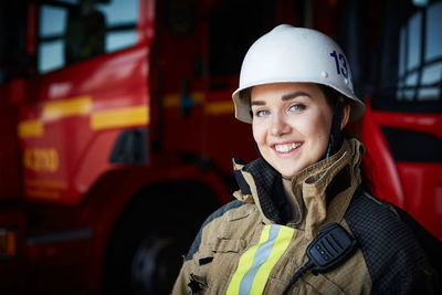 Portrait of smiling female firefighter in helmet at fire station