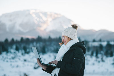 Rear view of man using mobile phone while standing against snowcapped mountain