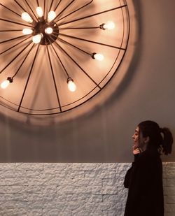 Low angle view of woman standing against illuminated ceiling