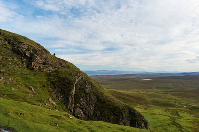 Tourist sitting mountain summit and watching over the landscape at quiraing isle of skye in scotland