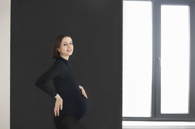 Portrait of young woman standing against window