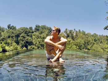 Full length of man sitting on rock in lake