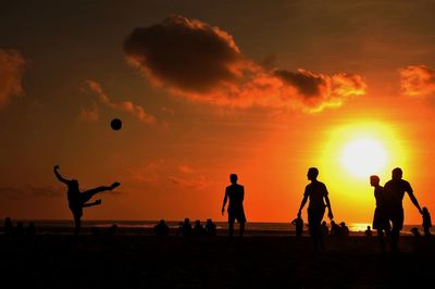 Silhouette people playing with ball at beach against sky during sunset