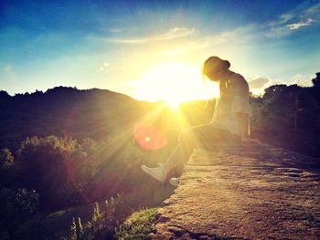 Man with arms raised on landscape against sky during sunset