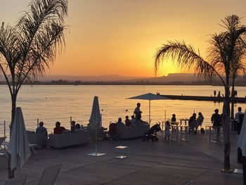 People in restaurant by sea against sky during sunset