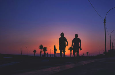 Silhouette people on street against orange sky