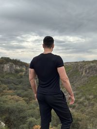 Rear view of man standing on mountain against sky