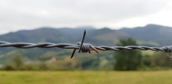Close-up of barbed wire fence on field against sky