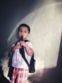Cute thoughtful schoolboy standing against wall