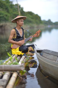 Full length of man playing guitar sitting on boat at lake