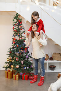 Happy mother carrying daughter on shoulders while standing by christmas tree