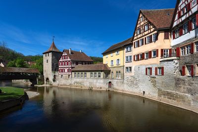 Footbridge over river by buildings against blue sky