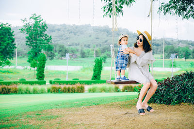 Cheerful mother sitting with son on swing at park