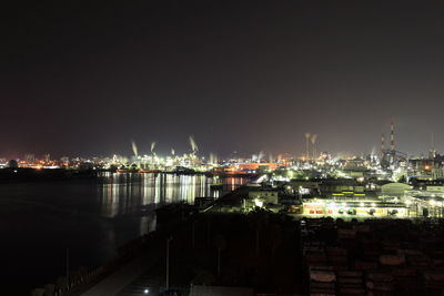 Illuminated cityscape by sea against clear sky at night