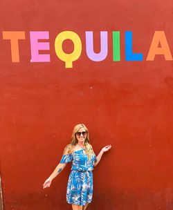 Young woman standing against wall with tequila text