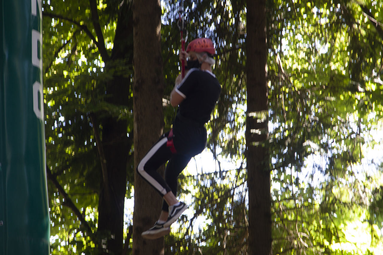 SIDE VIEW OF MAN CLIMBING ON TREE TRUNK