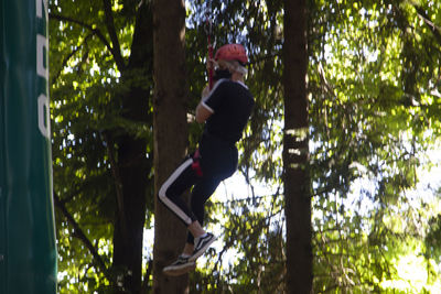 Side view of man climbing on tree trunk in forest