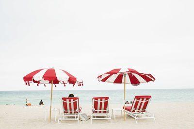 Lounge chairs and parasols at sea shore against clear sky