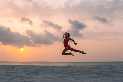 Man jumping over sea against sky during sunset