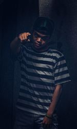 Portrait of young man standing against dark wall