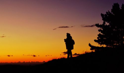 Silhouette of woman standing on landscape at sunset