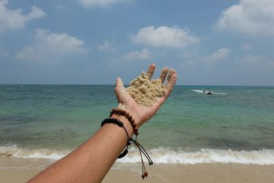 Cropped hand holding sand at beach against sky
