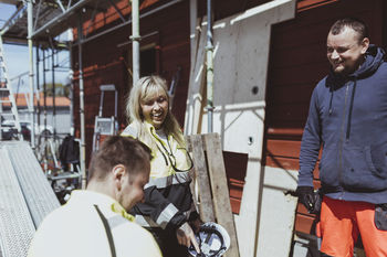 Happy male and female construction worker discussing together at site during sunny day