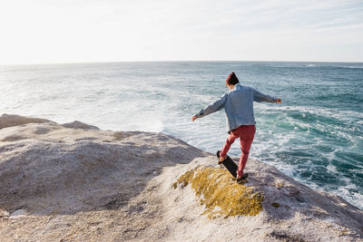 Rear view of boy on rock by sea against sky