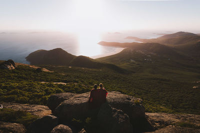 Rear view of couple sitting on rock against sky