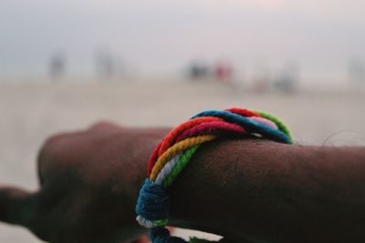 Close-up of human hand with multi colored band against the sky