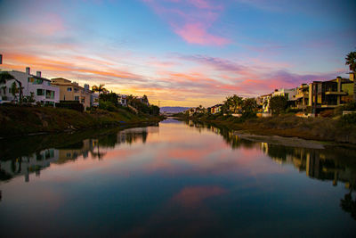 Scenic view of lake by buildings against sky during sunset