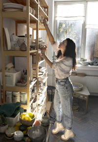 Young potter artisan at the ceramic studio. professional potter takes a handmade cup from the shelf.