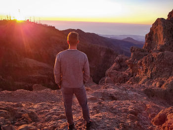 Rear view of man standing on rocky mountain during sunrise