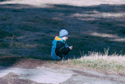 Boy wearing warm clothing while crouching on field