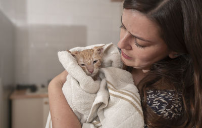 Woman carefully drying her little light brown baby kitten with a white towel after having bathed her