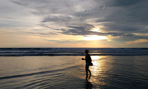 Silhouette man on beach against sky during sunset