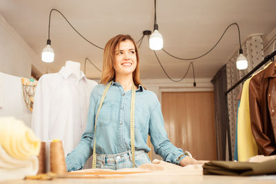 Portrait of seamstress woman in atelier. beautiful room, dummy with white shirt, counter with ready 