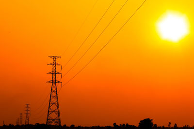 Low angle view of silhouette electricity pylon against orange sky