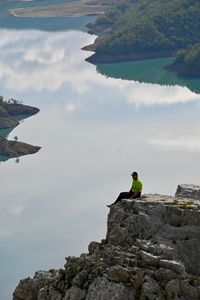 Man sitting on rock against sky